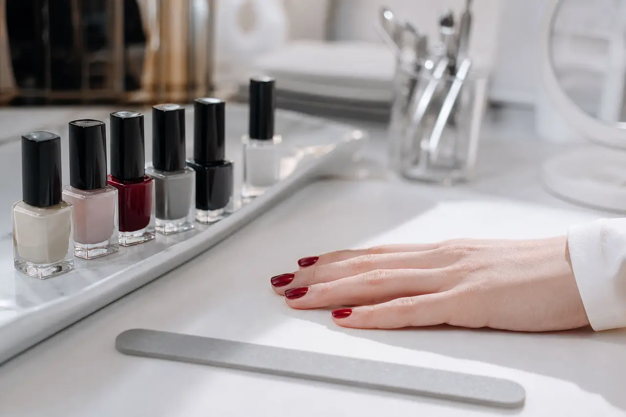 Hero Onglerie : Pose de vernis grenat sur ongle nu, gros plan mains, cadrage large cabine