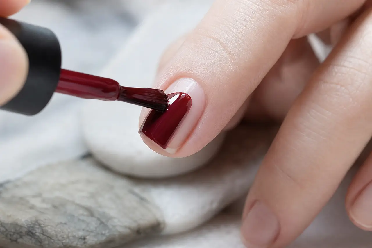 Pose de vernis grenat sur ongle nu, gros plan mains